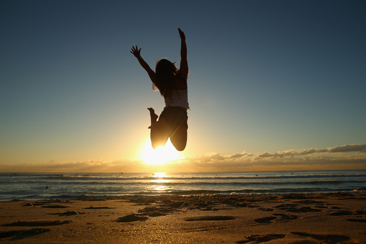 A woman jumps in the air on a beach at sunrise